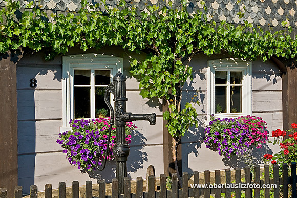 Foto von Peter Hennig PIXELWERKSTATT Detailaufnahme eines Umgebindehauses mit Wasserpumpe, Weinlaub und Blumenkästen
